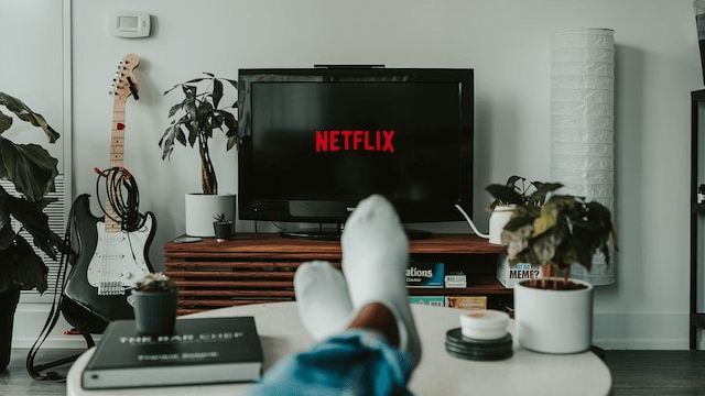 A person with their feet up on a coffee table in front of a TV screen that has the Netflix logo on it